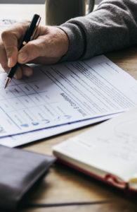 hand of a man with sweater signing health related documents with brian hall medicare consulting